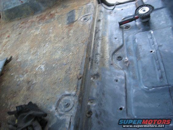 Vehicle floor being prepped with a grinder, showing rust and metal