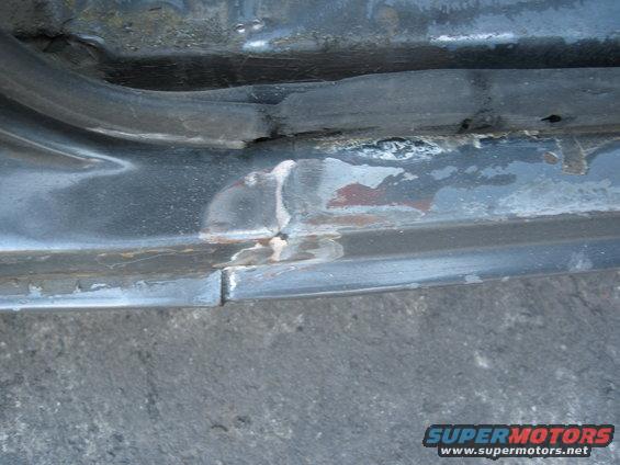 Close-up of a rusted metal door sill with a rubber seal