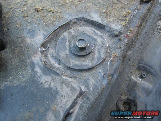 Close-up of a bolt and washer on a metal surface, likely a vehicle floor