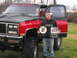 1991 GMC Jimmy - A man stands with a lifted red and black pickup truck, holding two awards, one of which indicates the year 1987.