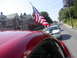 2004 Ford Mustang - A line of cars, including a white 2004 Ford Mustang, drive down a street with American flags displayed.