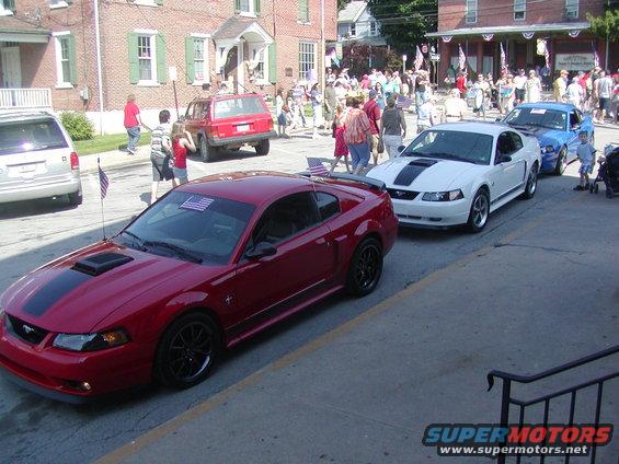 Red 2004 Ford Mustang with black racing stripes and black wheels parked on a street