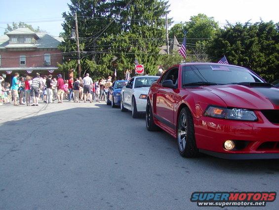 Red 2004 Ford Mustang in a parade with American flags