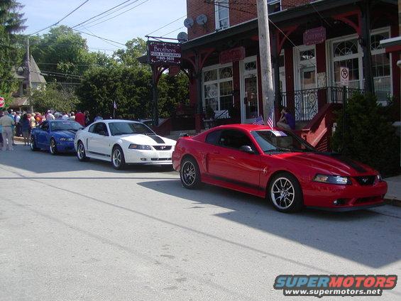 Red, white, and blue Mustangs parked on a street in front of a restaurant