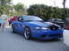 2004 Ford Mustang - A blue 2004 Ford Mustang with black racing stripes on the hood and aftermarket wheels is parked outdoors.