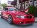 2004 Ford Mustang - Red 2004 Ford Mustang with black racing stripes parked in front of a building.