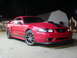 2004 Ford Mustang - A red 2004 Ford Mustang is parked outdoors at night, black racing stripes and an aftermarket hood scoop.