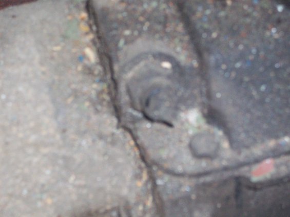 Close-up of a dirty, dark-colored mechanical part with a bolt head visible