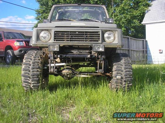 1987 Suzuki Samurai front view, lifted with large off-road tires. Red SUV parked behind it