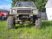 1987 Suzuki Samurai - Modified 1987 Suzuki Samurai parked in grass, showing its lifted suspension and large tires.