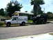 2000 Ford F-250 - A white pickup truck tows a trailer with a black truck on it down a residential street.