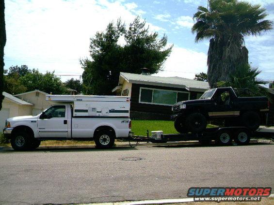 White 2000 Ford F-250 with camper towing a black truck on a trailer