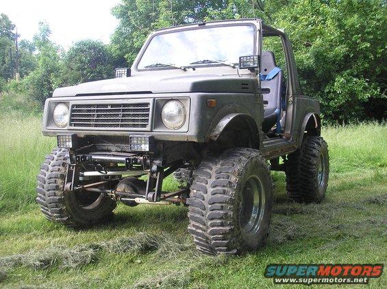 1987 Suzuki Samurai modified with a lift kit and oversized off-road tires, parked in a grassy field