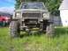 1987 Suzuki Samurai - This heavily modified vehicle has oversized tires and a lifted suspension, parked in a grassy yard.