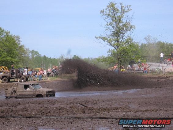 Muddy truck driving through a mud pit with spectators watching