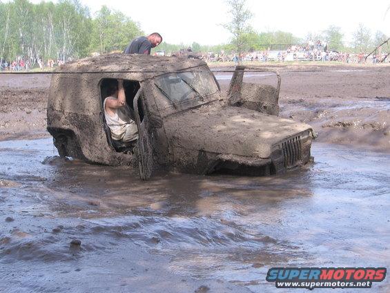 Mud-covered Jeep Wrangler stuck in mud with people inside and on top