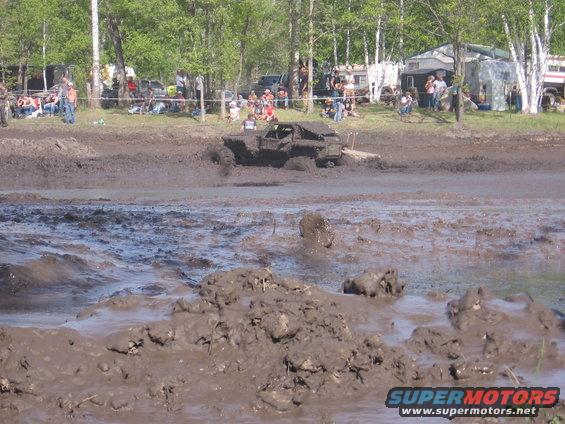 Mud-covered off-road truck driving through a muddy track with spectators in the background