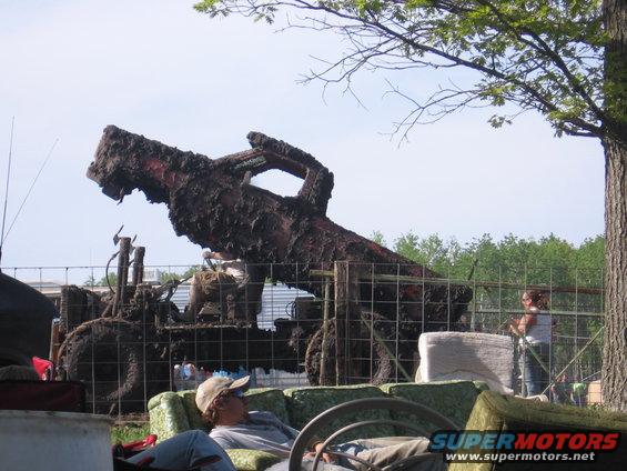 Mud-covered tractor with large exhaust pipe angled upwards, behind a fence
