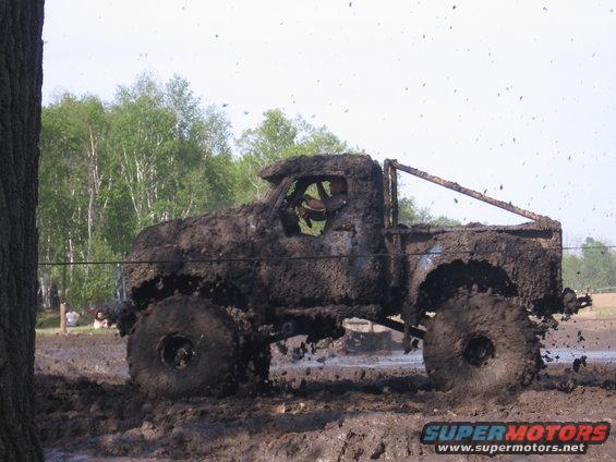 Muddy old truck with big tires driving through a mud pit, throwing mud everywhere