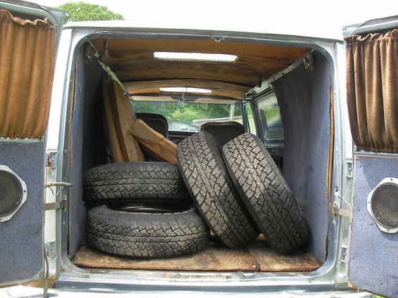 Van interior with four tires and wooden planks stacked inside. Brown curtains hang on the sides