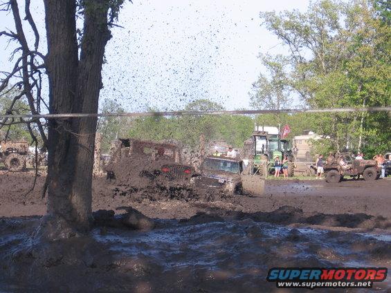Vehicles stuck in mud, with a tractor in the background