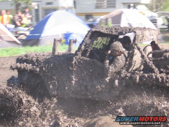 mud-covered off-road vehicle with occupants splashing through mud