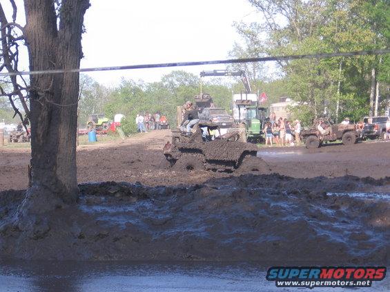 Trucks and ATVs stuck in mud at an outdoor event with spectators watching