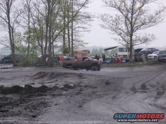 Red pickup truck stuck in mud at an outdoor event
