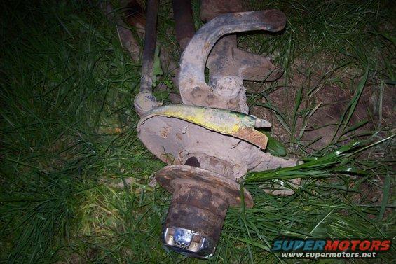 Rusty truck suspension part with yellow and green paint remnants, lying in grass