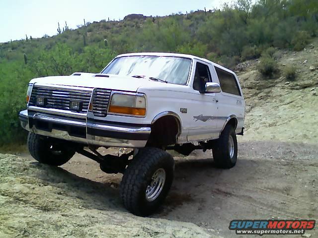 White Ford Bronco with lifted suspension on a dirt trail, front 3/4 view
