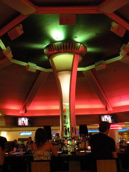 Interior of a bar with people sitting at the counter, under colorful ceiling lights