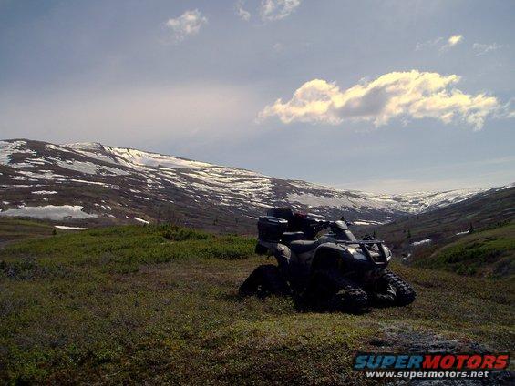 Four-wheeler ATV parked in grassy field with snow-capped mountains in background