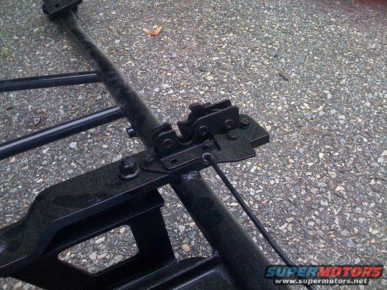 close-up of black metal frame parts and a latch assembly on asphalt