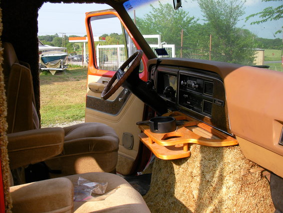 Interior view of a 1978 Ford E150 van, showing the driver's seat, dashboard, and a custom wooden console with a cup holder
