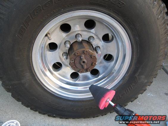 Polishing cone attached to a drill polishes a chrome wheel with a rusty hub. Tire has "BFGOODRICH" text