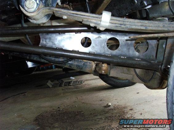 Undercarriage view of truck suspension with leaf springs and differential. Visible "SUPERMOTORS" logo