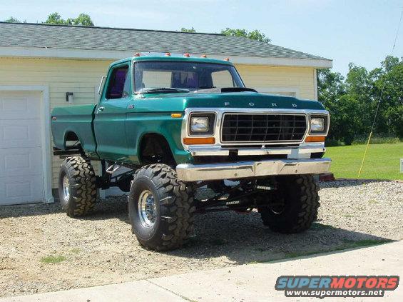 Green 1979 Ford F-100 pickup truck with large tires and lifted suspension parked in front of a garage