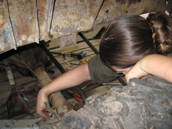Person working on the rusty undercarriage of a vehicle, near a large tire