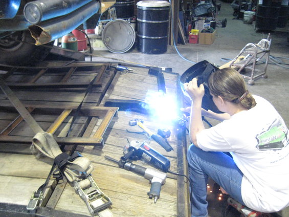 Person welding on a trailer with tools and barrels in background