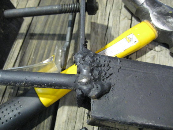 Welded black metal bracket with bolts and a yellow tool handle