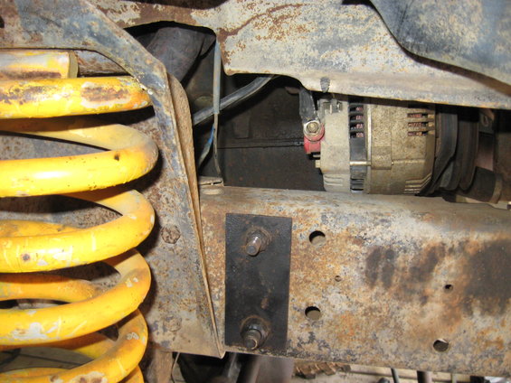 Close-up of rusty vehicle frame with yellow coil spring and alternator