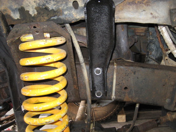 Close-up of yellow coil spring and black suspension bracket on rusty frame