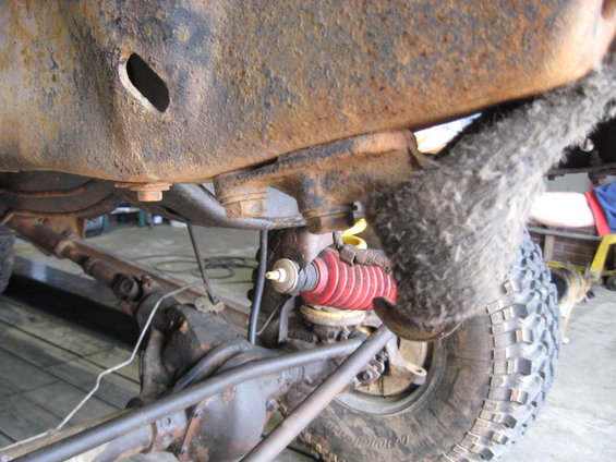 Close-up of rusty vehicle frame with red shock absorber and tire visible