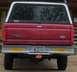 2006 Ford E350 - Rear view of a red Ford F350 pickup truck with a white camper shell and various bumper stickers.