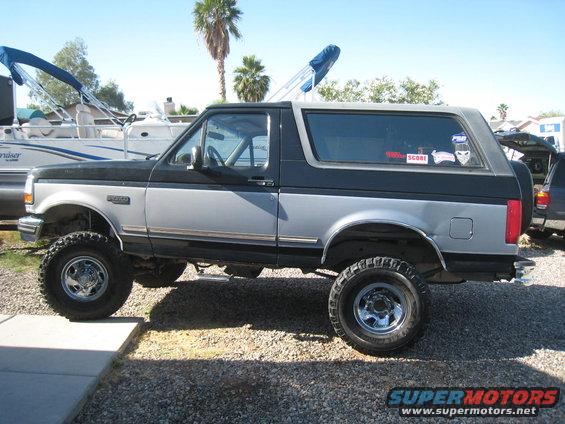 Two-tone black and silver lifted Ford Bronco with aftermarket wheels, parked on gravel