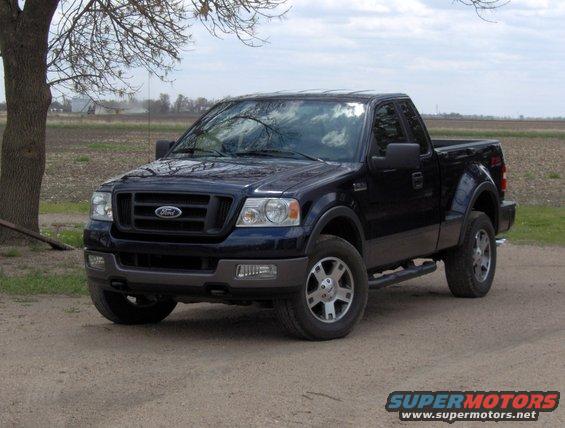 Dark blue Ford F-150 pickup truck parked on a dirt road near a field