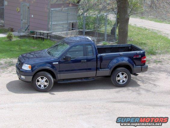 Blue Ford F-150 pickup truck, 3/4 front view, parked on a dirt road