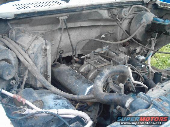 Engine bay with visible hoses and engine components. Watermark reads SUPERMOTORS