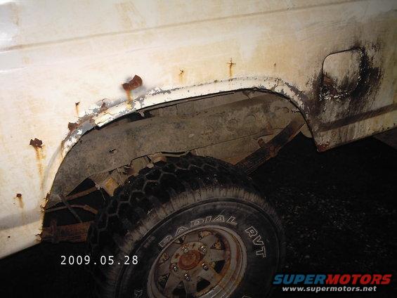 White SUV rear wheel well with significant rust and damage. Tire is visible