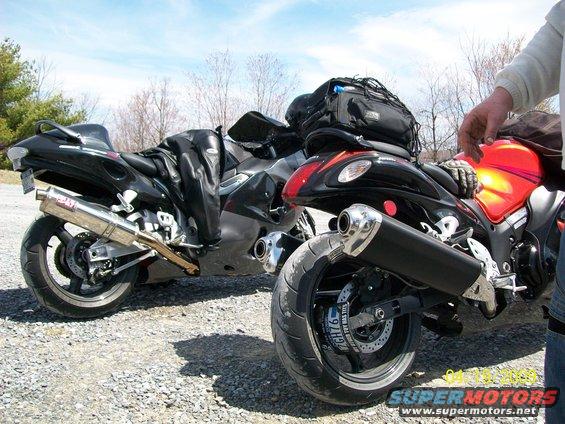 Two Suzuki Hayabusa motorcycles parked on a gravel lot. One is black, the other has a red tank